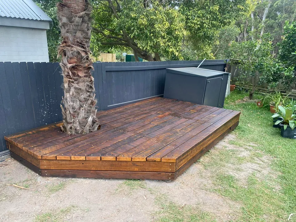 Compact hardwood platform deck wrapped around mature palm in backyard