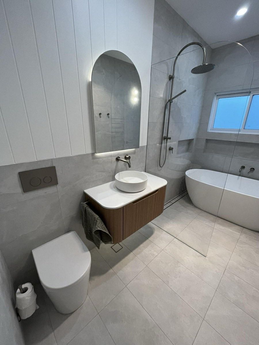 Modern bathroom with arched mirror, freestanding tub and timber fluted vanity